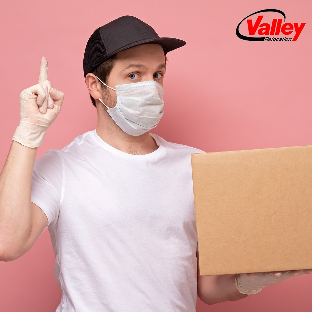 Professional mover holding a box with a mask on his face  