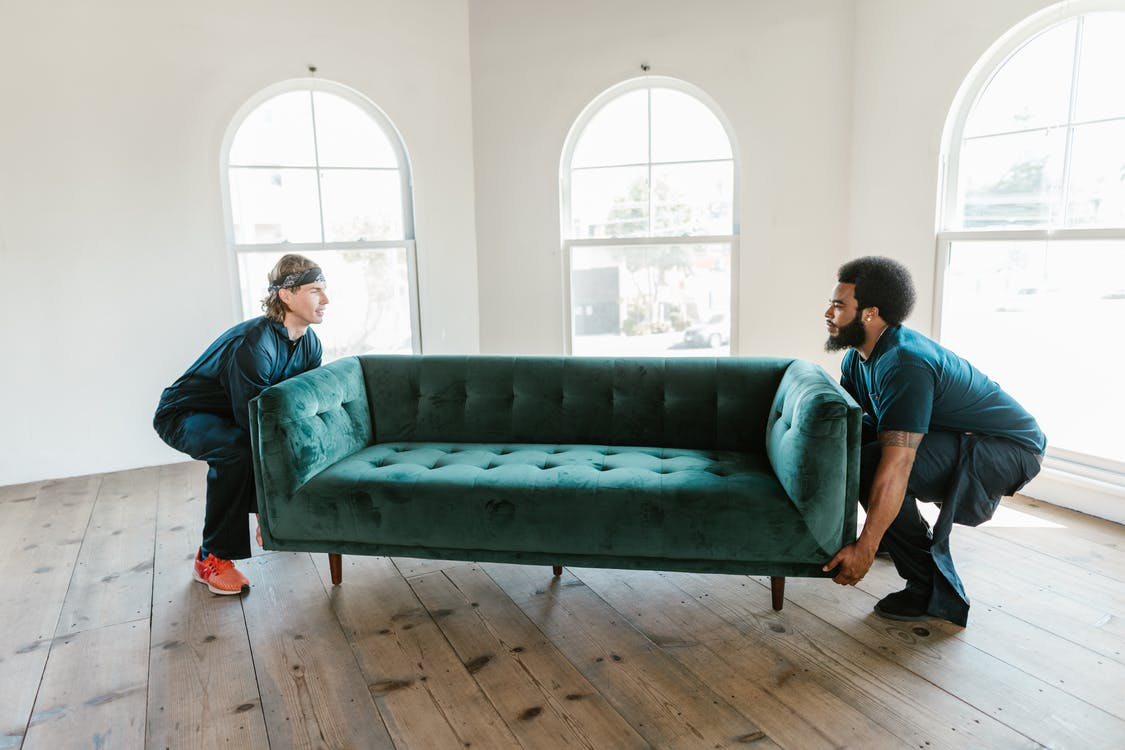 Two movers lifting a green sofa off the ground