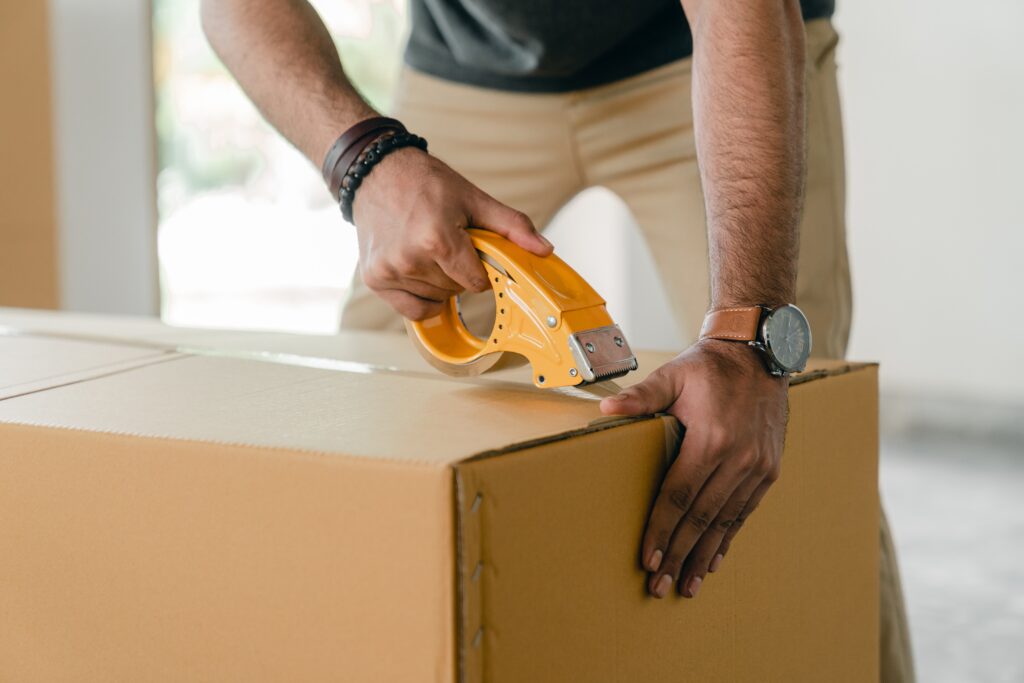 A person packing a cardboard box with tape.