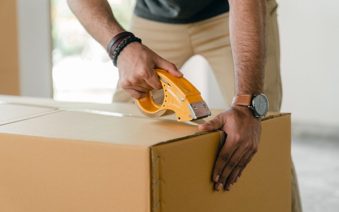 A person packing a cardboard box with tape.