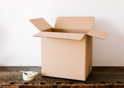 A cardboard box laying on a wooden surface with tape and scissors next to it