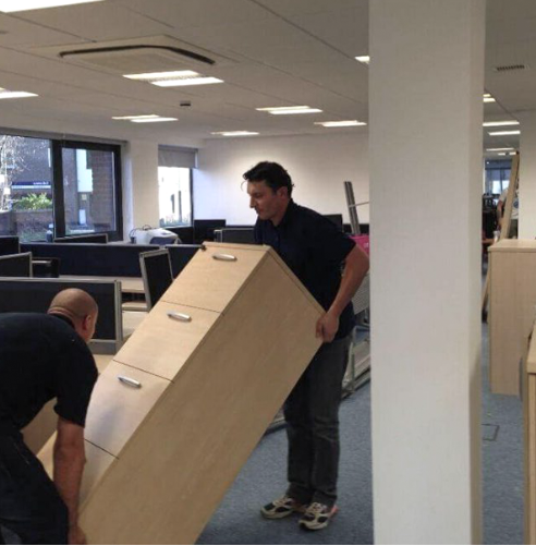 Two people moving an office cabinet across the floor.