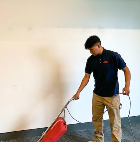 A uniformed person vacuuming floors of an empty office. 