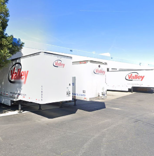  Different types of white moving vans are all parked in an open space parking lot. 