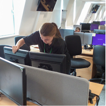 A person moving around equipment and boxes in an open space. 