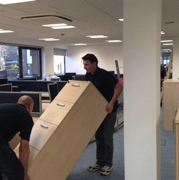 Two people moving the shelves across a room. 