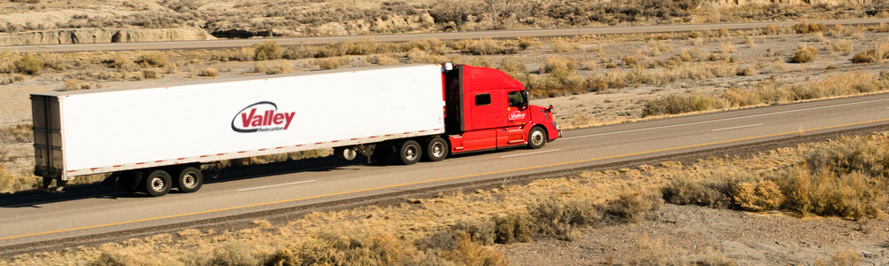 A red and white moving van driving across a highway. 