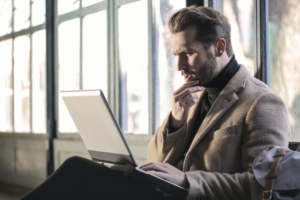 A suited man sitting and thinking about something on his laptop.