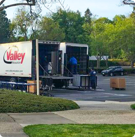 A large moving truck parked in the parking lot with a person loading boxes. 