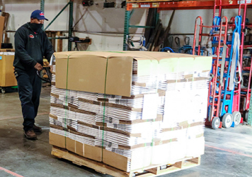 A person pushing a cart full of cardboard boxes.