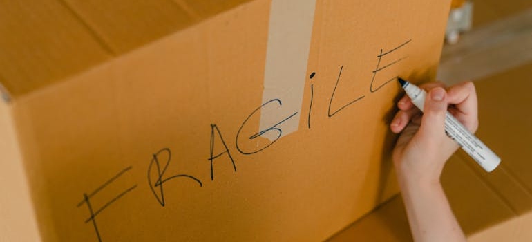 Person labeling a box with a word fragile, preparing it for a storage Concord CA