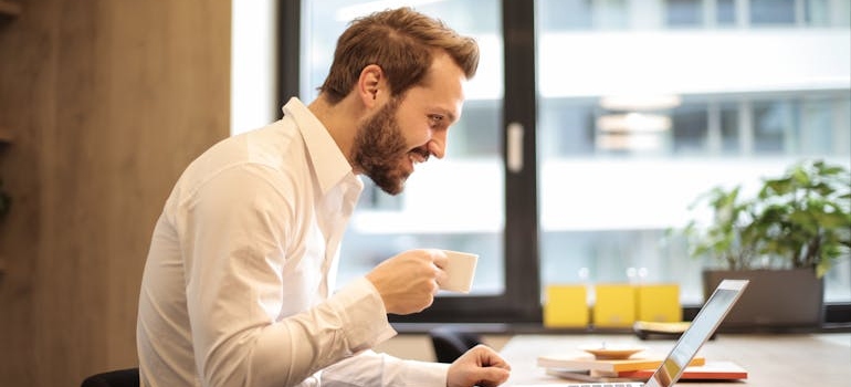 Man looking at a laptop and drinking coffee.