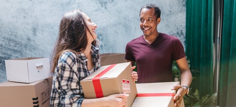 Two people laughing and carrying boxes.