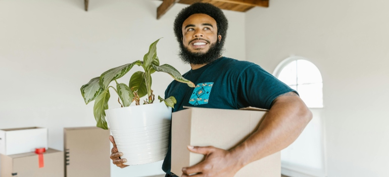 A smiling mover holding a plant and a box, ready to assist with your move in San Ramon.