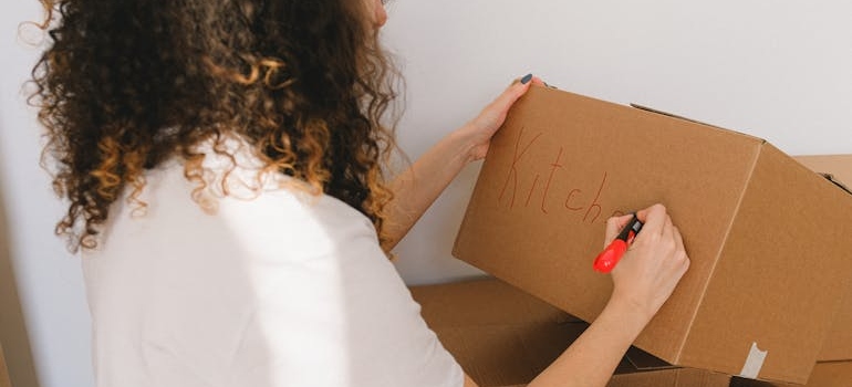 Woman labeling a cardboard box before the long distance movers Bay Area arrive.