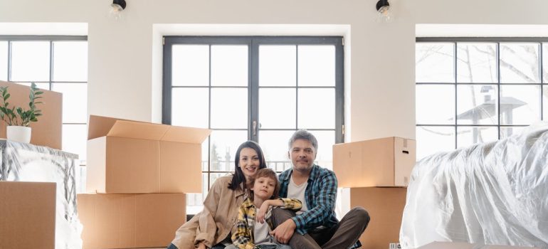 family of three sitting on floor surrounded by moving boxes