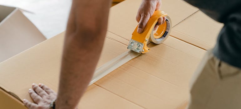 Man using scotch tape to shut a cardboard box.