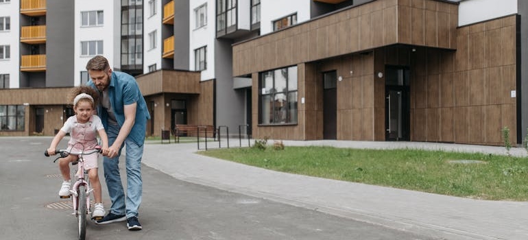 Father teaching his daughter to ride a bicycle in their new neighborhood to make moving with kids easier.