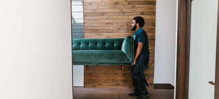 Man carrying a couch out of an apartment.