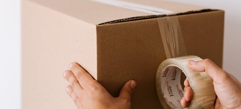 man sealing cardboard container with tape