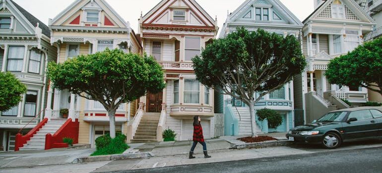 Woman Walking Toward Black Sedan Parked In Front of Colorful Houses
